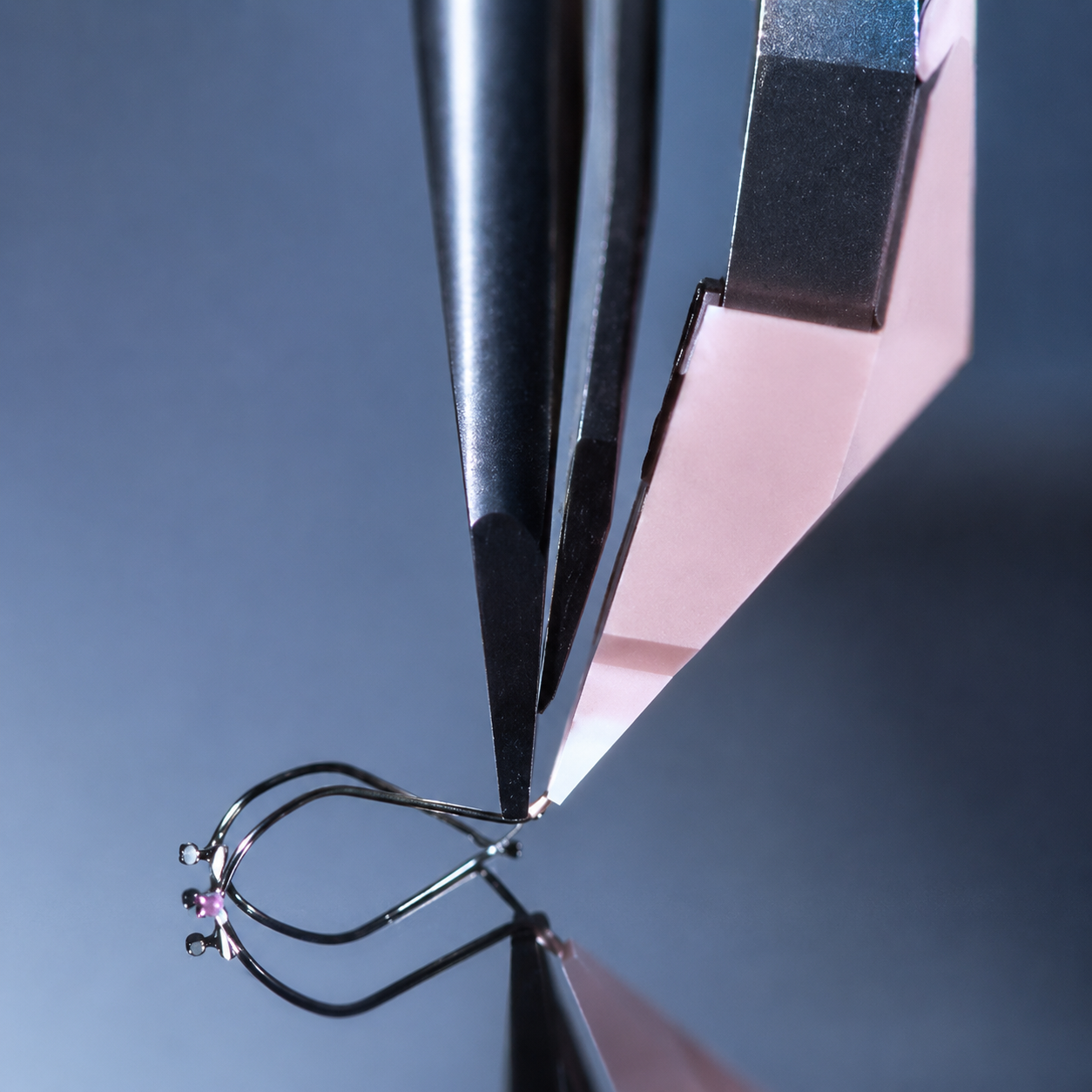 Precision tweezers positioning a miniature optical component with fine gold leads during photonic assembly